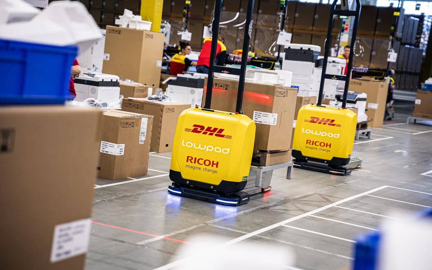 Lowpad-robots rijden zelfstandig door het DHL-magazijn langs pallets met dozen