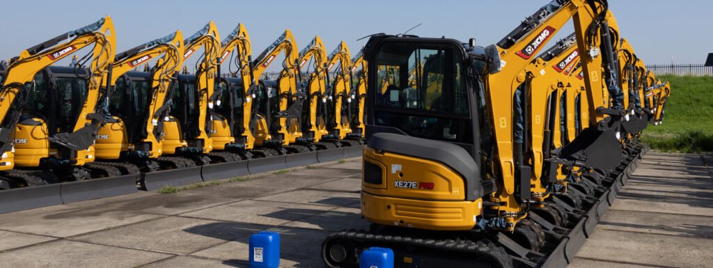 Lange rij gele minigraafmachines op een terrein, met één machine op de voorgrond